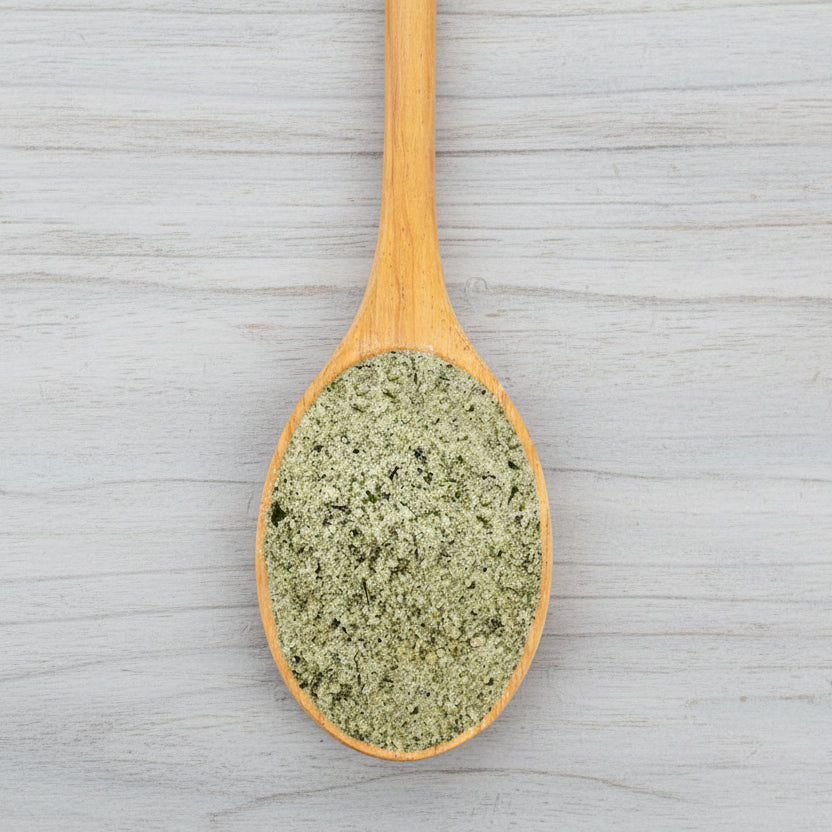 Wooden spoon filled with green spice mix on a white background